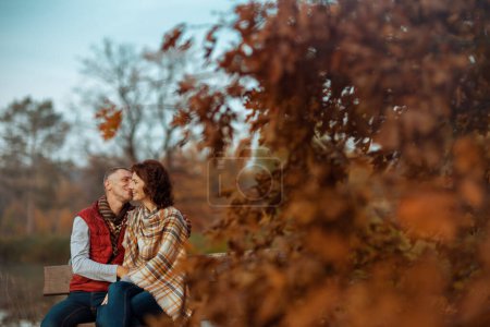 Foto de Hola otoño. sonriente pareja moderna en el parque besándose mientras está sentado en el banco. - Imagen libre de derechos