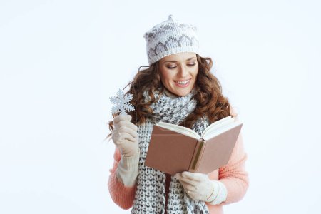 Foto de Hola invierno. sonriente mujer moderna en suéter, mitones, sombrero y bufanda con copo de nieve y libro aislado en blanco. - Imagen libre de derechos