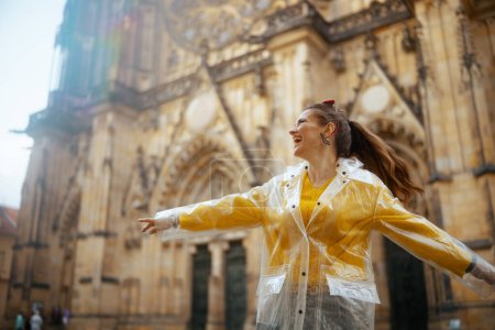 Photo for Happy middle aged traveller woman in yellow blouse and raincoat in Prague Czech Republic enjoying promenade. - Royalty Free Image