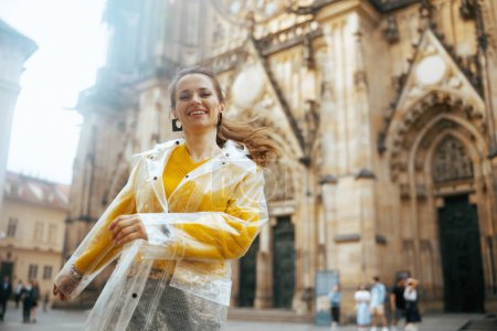 Photo for Happy trendy middle aged traveller woman in yellow blouse and raincoat in Prague Czech Republic enjoying promenade. - Royalty Free Image