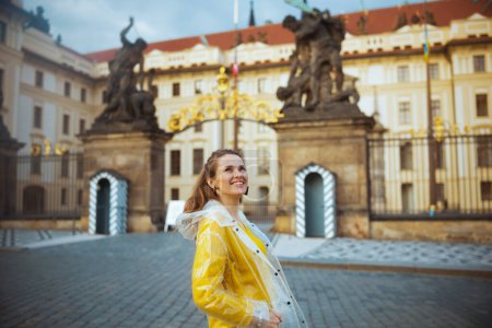 lächelnde, stilvolle Reiseleiterin in gelber Bluse und Regenmantel in Prag.