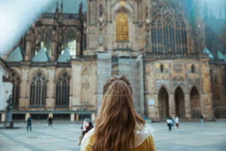 Foto de Visto desde atrás viajero mujer en blusa amarilla y impermeable en Praga República Checa explorar atracciones. - Imagen libre de derechos
