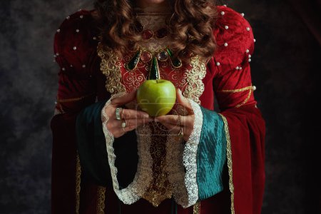 Foto de Primer plano de la reina medieval en vestido rojo con manzana verde sobre fondo gris oscuro. - Imagen libre de derechos