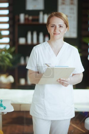 Photo for Healthcare time. Portrait of smiling massage therapist woman in spa salon with clipboard. - Royalty Free Image