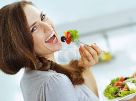 Photo for Smiling young woman eating fresh salad in modern kitchen - Royalty Free Image