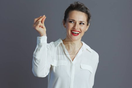 Téléchargez les photos : Souriant tendance 40 ans femme d'affaires en chemisier blanc doigts claquant isolé sur fond gris. - en image libre de droit