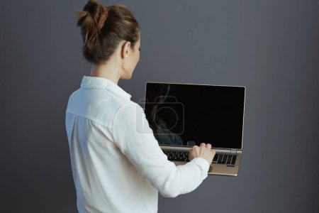 Téléchargez les photos : Vu de derrière femme ouvrière en chemisier blanc à l'aide d'un ordinateur portable isolé sur fond gris. - en image libre de droit
