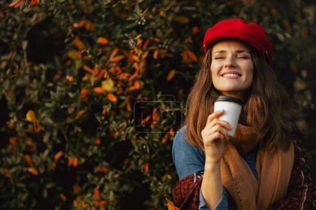 Photo for Hello autumn. smiling young woman in red hat with autumn leafs, scarf and coffee in the city park. - Royalty Free Image