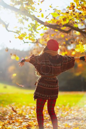 Photo for Hello autumn. Seen from behind female in red hat with scarf and gloves rejoicing in the city park. - Royalty Free Image