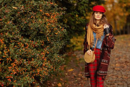 Photo for Hello autumn. Portrait of happy trendy female in jeans shirt and red hat with scarf, gloves and bag in the city park. - Royalty Free Image