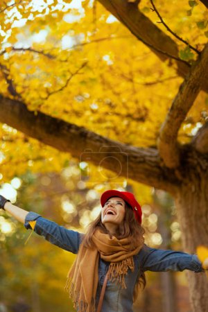 Foto de Hola otoño. feliz joven con camisa vaquera y sombrero rojo con bufanda regocijándose en el parque de la ciudad. - Imagen libre de derechos
