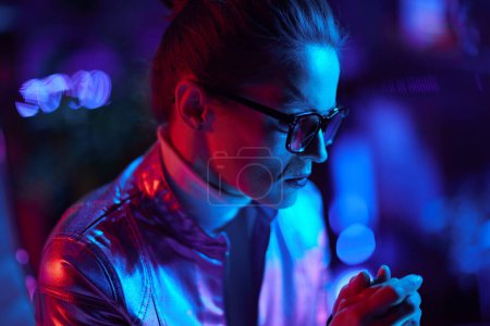 Photo for Neon metaverse futuristic concept. pensive stylish 40 years old woman in glasses in modern office. - Royalty Free Image