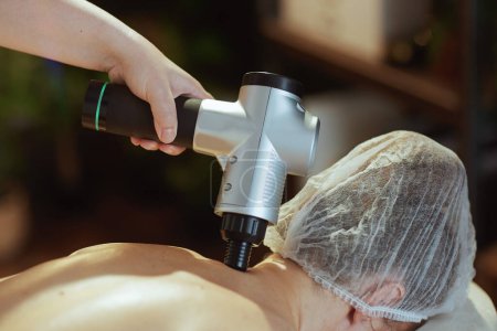 Photo for Healthcare time. Closeup on medical massage therapist in spa salon with massage pistol massaging clients neck. - Royalty Free Image