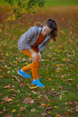 Photo for Hello autumn. sad elegant woman in fitness clothes in the park having leg pain. - Royalty Free Image