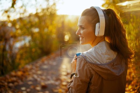 Photo for Hello autumn. smiling elegant woman in fitness clothes in the park listening to the music with headphones. - Royalty Free Image