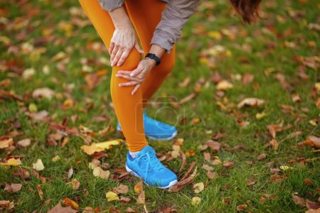 Photo for Hello autumn. Closeup on middle aged woman in fitness clothes in the park with knee pain. - Royalty Free Image