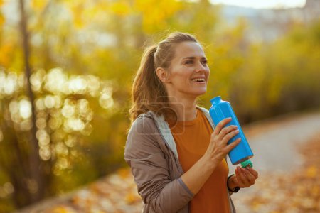 Téléchargez les photos : Bonjour l'automne. heureuse femme d'âge moyen à la mode en vêtements de fitness dans le parc avec bouteille d'eau. - en image libre de droit