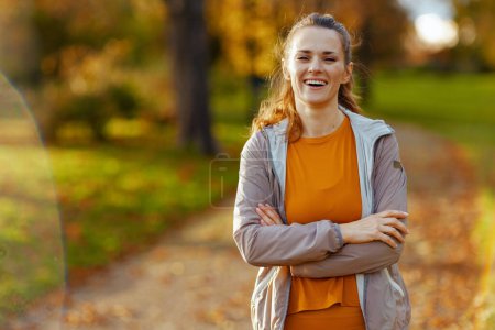 Téléchargez les photos : Bonjour l'automne. Portrait de femme moderne souriante en vêtements de fitness dans le parc se détendre après l'entraînement. - en image libre de droit