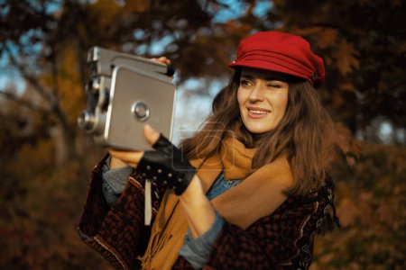 Photo for Hello autumn. stylish female in red hat with retro video camera, scarf and gloves in the city park. - Royalty Free Image