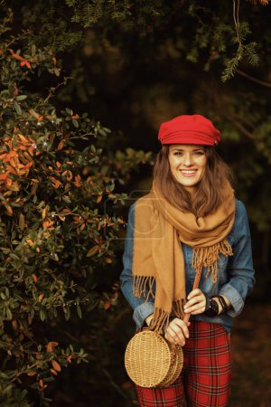 Téléchargez les photos : Bonjour l'automne. femme moderne souriante en jeans chemise et chapeau rouge avec écharpe, gants et sac dans le parc de la ville. - en image libre de droit