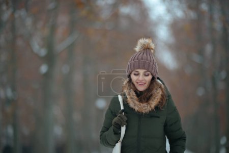 Foto de Feliz mujer moderna de mediana edad en abrigo verde y sombrero marrón al aire libre en el parque de la ciudad en invierno con gorro sombrero. - Imagen libre de derechos