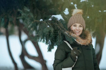 Foto de Mujer moderna feliz en abrigo verde y sombrero marrón al aire libre en el parque de la ciudad en invierno con manoplas y gorro sombrero. - Imagen libre de derechos