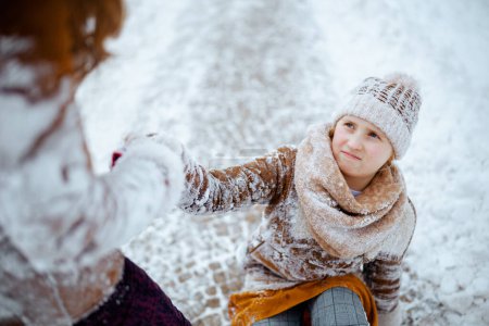 Téléchargez les photos : Mère aidant fille se lever après être tombé à l'extérieur dans le parc de la ville en hiver. - en image libre de droit