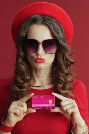 Téléchargez les photos : Joyeux Valentin. élégante femme d'âge moyen en robe rouge et béret sur fond rouge avec carte de crédit. - en image libre de droit