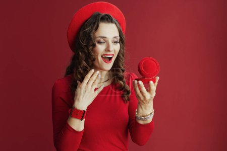 Téléchargez les photos : Joyeux Valentin. excité femme d'âge moyen élégant en robe rouge et béret sur fond rouge avec boîte à bijoux. - en image libre de droit