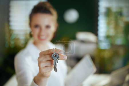 Photo for Time to move on. Closeup on modern 40 years old woman realtor in modern green office in white blouse with keys. - Royalty Free Image