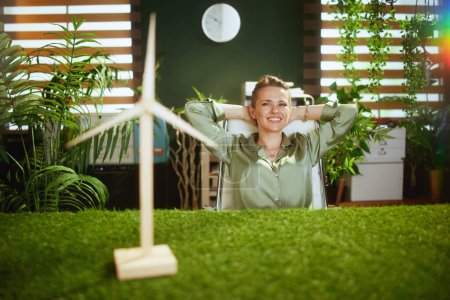 Foto de Relajado 40 años de edad mujer de negocios en blusa verde en moderna oficina verde con molino de viento - Imagen libre de derechos