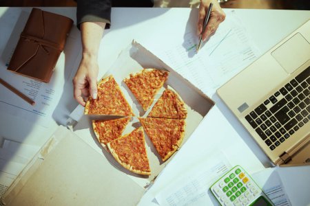 Téléchargez les photos : Un lieu de travail durable. Vue supérieure de l'employée dans un bureau vert avec pizza et ordinateur portable. - en image libre de droit
