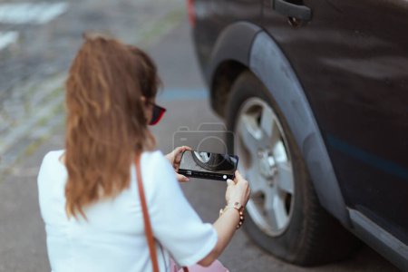Téléchargez les photos : Accident de voiture. Gros plan sur voyageuse femme dans la ville avec smartphone près de la voiture avec pneu crevé. - en image libre de droit