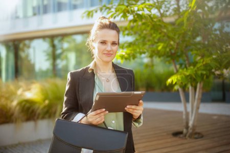Téléchargez les photos : Travailleur femme moderne dans le quartier des affaires en veste noire avec mallette en utilisant tablette PC. - en image libre de droit