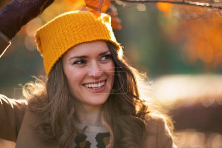 Photo for Hello october. happy trendy female in beige coat and orange hat outside on the city park in autumn. - Royalty Free Image