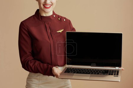 Téléchargez les photos : Gros plan sur femme hôtesse de l'air moderne isolé sur fond beige montrant écran blanc ordinateur portable. - en image libre de droit