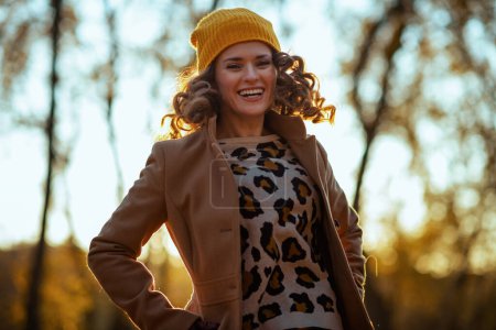 Photo for Hello october. smiling elegant female in beige coat and orange hat jumping outside on the city park in autumn. - Royalty Free Image