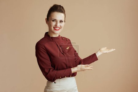 Téléchargez les photos : Souriant élégante hôtesse de l'air féminin sur fond beige accueillant. - en image libre de droit