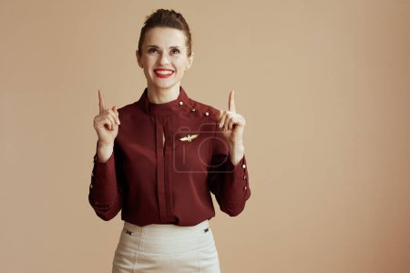 Photo for Happy elegant air hostess woman on beige background pointing up at copy space. - Royalty Free Image