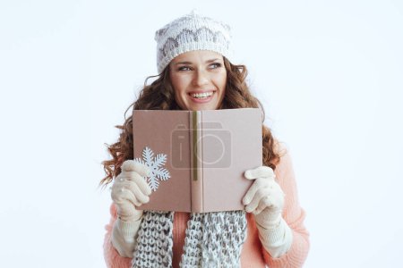 Photo for Hello winter. smiling trendy middle aged woman in sweater, mittens, hat and scarf isolated on white background with snowflake and book. - Royalty Free Image