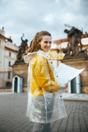 Photo for Happy stylish solo tourist woman in yellow blouse and raincoat in Prague Czech Republic with map near Prague Castle. - Royalty Free Image
