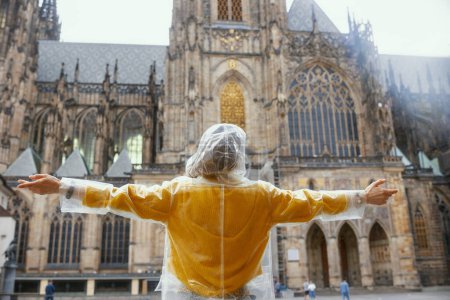 Foto de Visto desde atrás mujer en blusa amarilla y impermeable en Praga República Checa disfrutando de paseo marítimo y regocijo. - Imagen libre de derechos