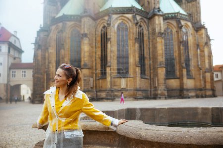 Foto de Feliz mujer turista de moda en blusa amarilla y impermeable en Praga República Checa teniendo excursión. - Imagen libre de derechos