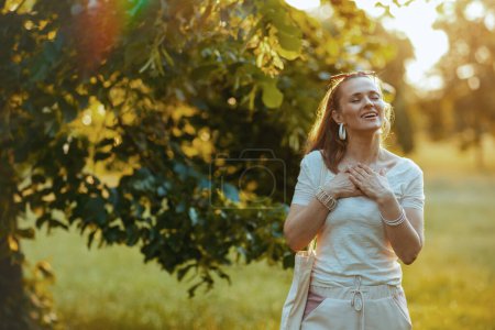 Foto de Hora de verano. mujer de moda feliz en camisa blanca con la mano en el pecho en el parque de la ciudad. - Imagen libre de derechos