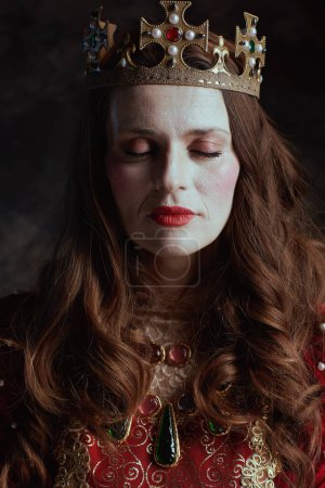 Photo for Medieval queen in red dress with white makeup and crown on dark gray background. - Royalty Free Image