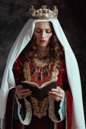 Photo for Medieval queen in red dress with book, veil and crown on dark gray background. - Royalty Free Image