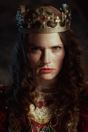 Photo for Medieval queen in red dress with crown on dark gray background. - Royalty Free Image