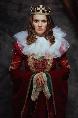 Foto de Reina medieval en vestido rojo con cuello blanco y corona sobre fondo gris oscuro. - Imagen libre de derechos