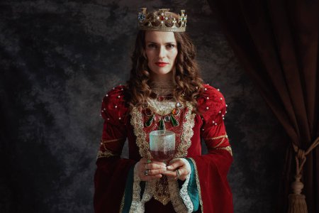 Foto de Reina medieval en vestido rojo con copa y corona sobre fondo gris oscuro. - Imagen libre de derechos