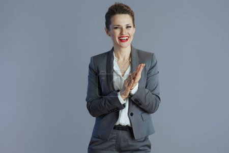 happy elegant woman worker in grey suit applauding isolated on gray background.